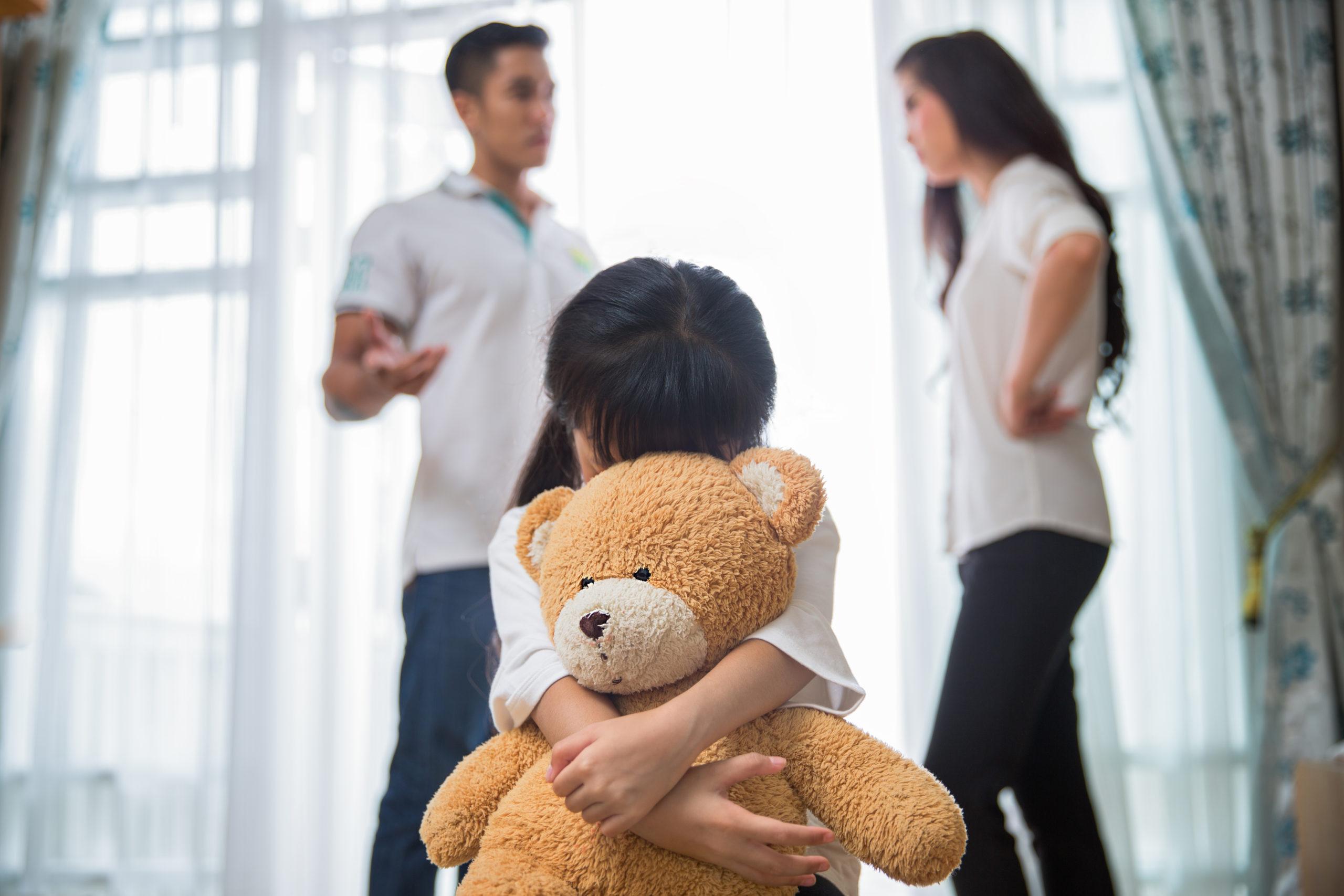 child hugging bear as parents argue